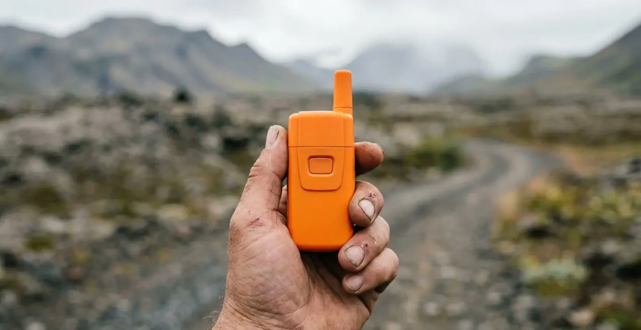 Main tenant une balise de détresse orange dans un paysage de haute terre islandaise désertique