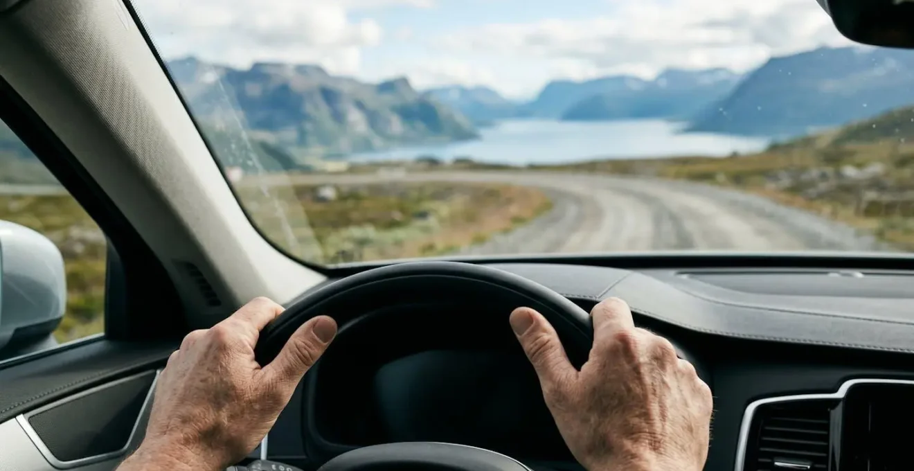 Mains sur le volant d'un véhicule traversant une route de gravier étroite avec vue sur un fjord en contrebas