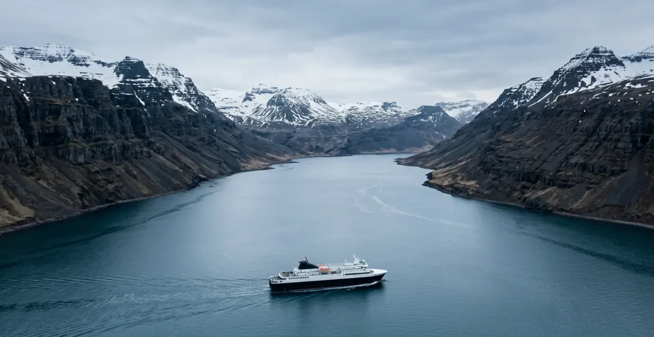 Vue panoramique depuis le pont d'un ferry islandais naviguant dans un fjord majestueux avec montagnes enneigées