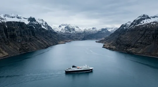 Vue panoramique depuis le pont d'un ferry islandais naviguant dans un fjord majestueux avec montagnes enneigées
