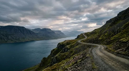 Route sinueuse serpentant le long d'un fjord islandais entouré de montagnes escarpées sous un ciel changeant