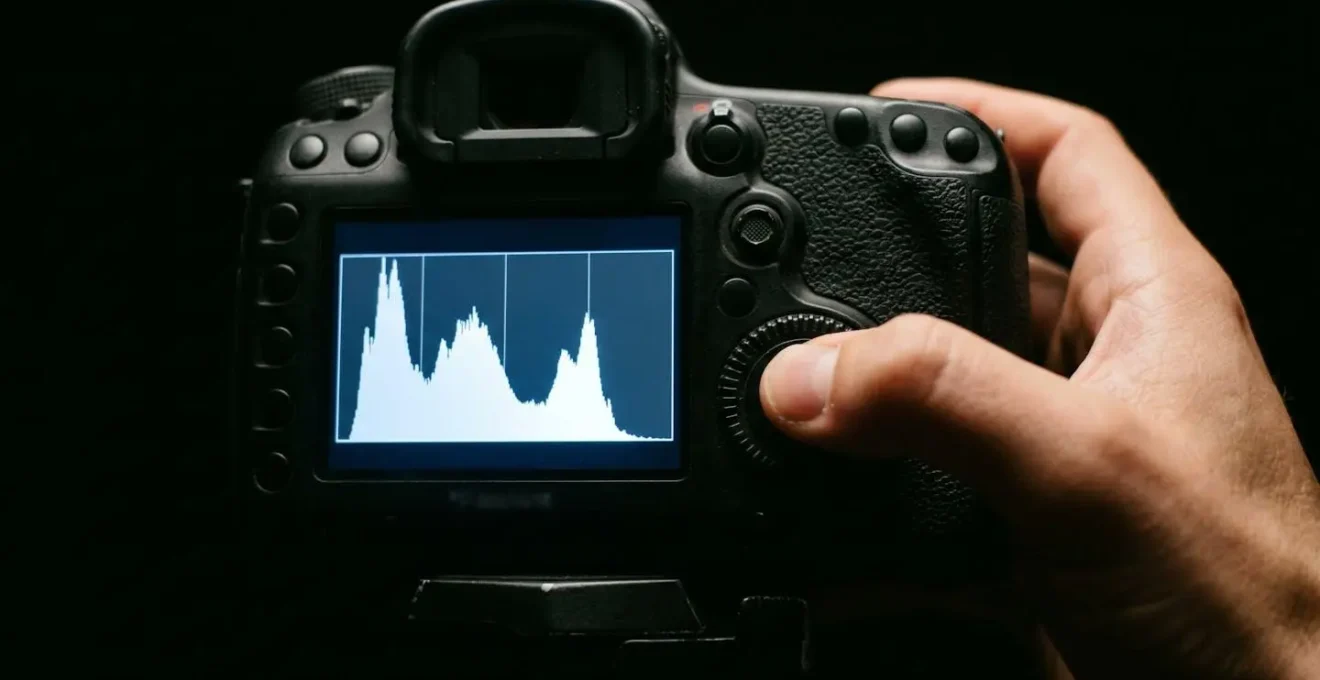 Écran LCD d'appareil photo affichant un histogramme d'exposition avec des pics équilibrés, photographe ajustant les réglages dans l'obscurité