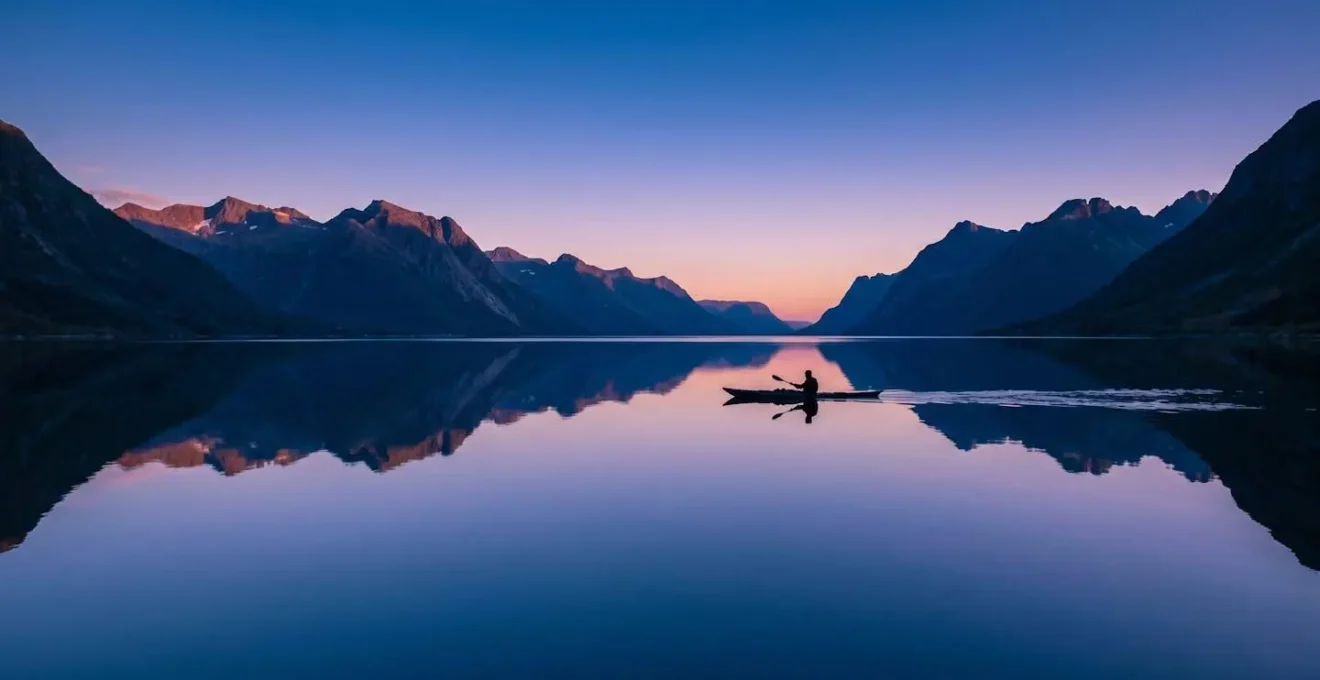 Kayakiste sur des eaux parfaitement calmes reflétant les couleurs du crépuscule et les montagnes environnantes