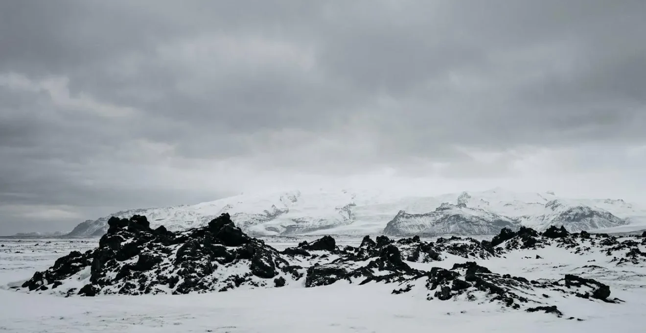 Paysage volcanique islandais montrant des formations de basalte noir contrastant avec la neige blanche sous une lumière dramatique