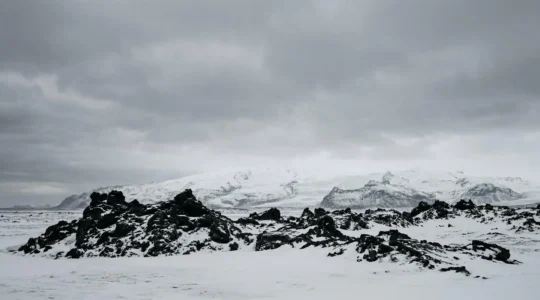 Paysage volcanique islandais montrant des formations de basalte noir contrastant avec la neige blanche sous une lumière dramatique