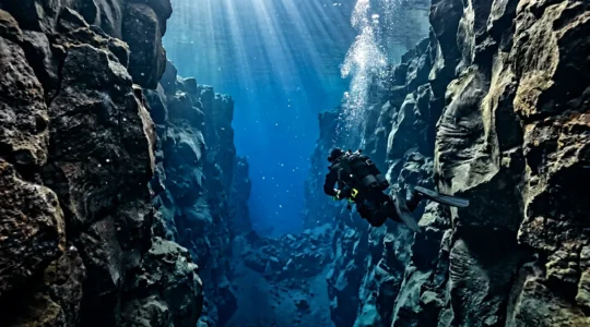Plongeur dans une combinaison étanche naviguant entre les parois rocheuses d'une faille sous-marine cristalline en Islande